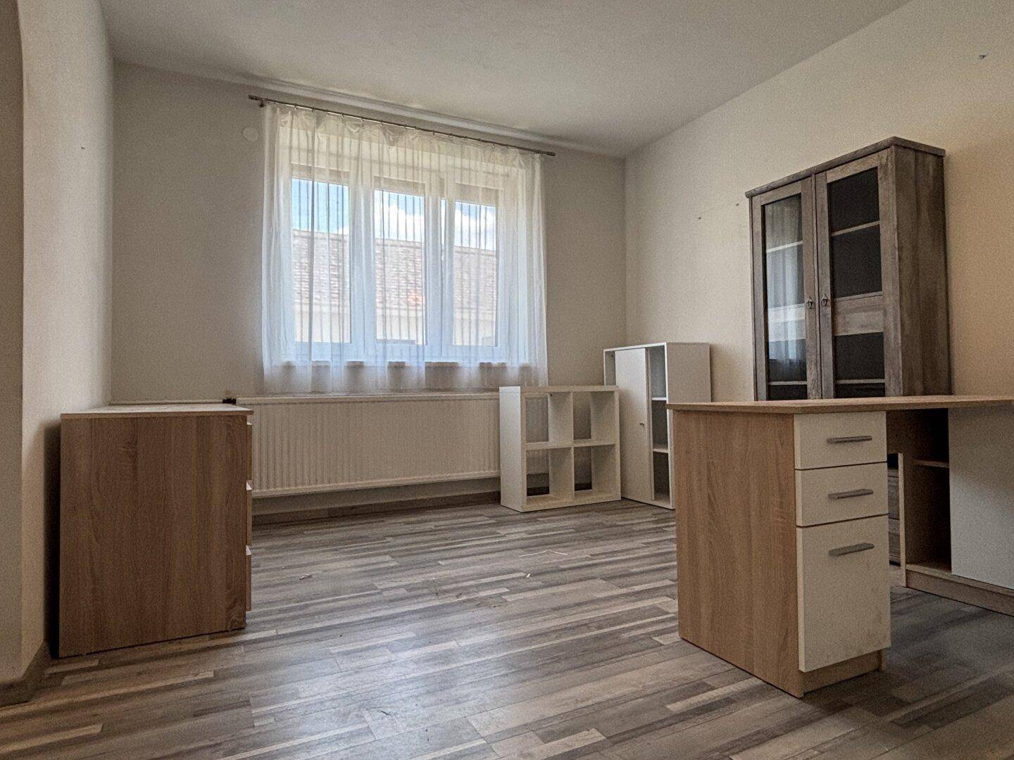 Helles Arbeitszimmer mit Laminatboden, großem Fenster und einfacher Büroeinrichtung.