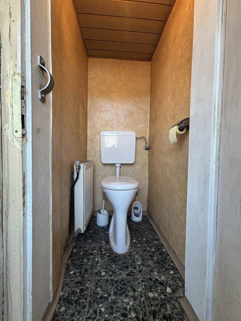 Kleines Gäste-WC mit dunklem Fliesenboden und einfacher Toilette.