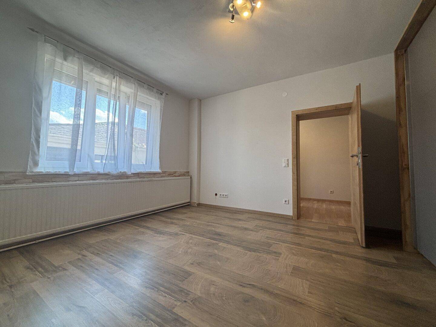 Helles Schlafzimmer mit neuem Laminatboden und großem Fenster, bereit zur Einrichtung.