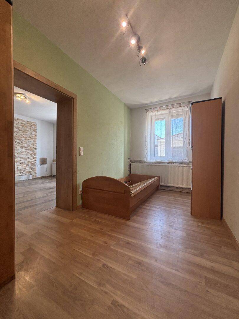 Einfaches Schlafzimmer mit Holzbett, Laminatboden und grün gestrichener Wand.