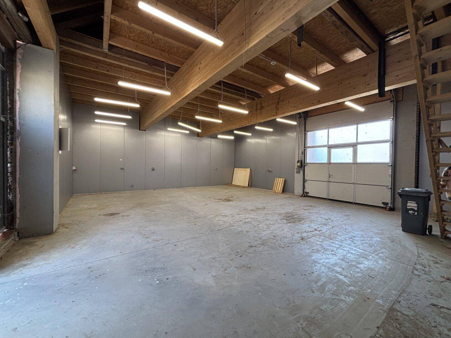Geräumige Garage mit hohen Decken, Holzbalken und großem Rolltor.