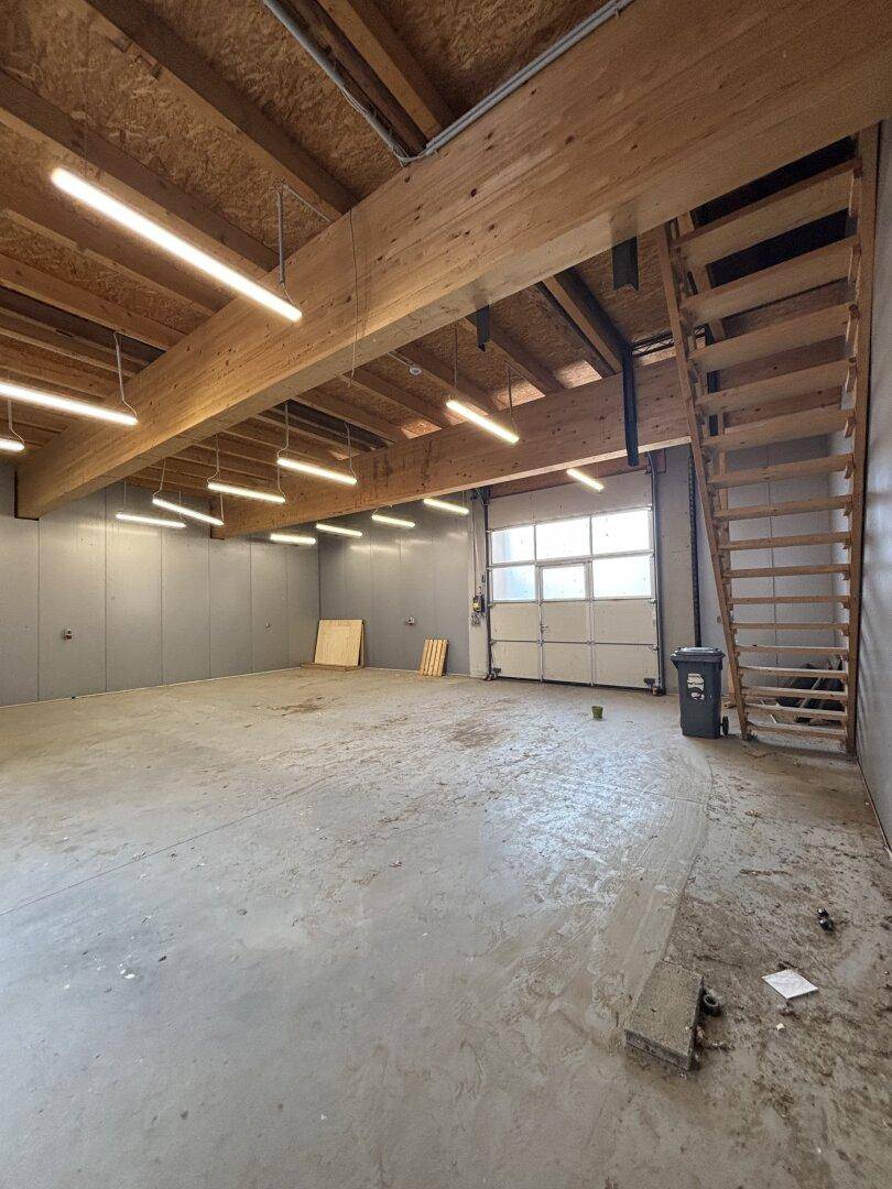 Große, helle Garage mit Betonboden, Holzbalken und einer Holztreppe.