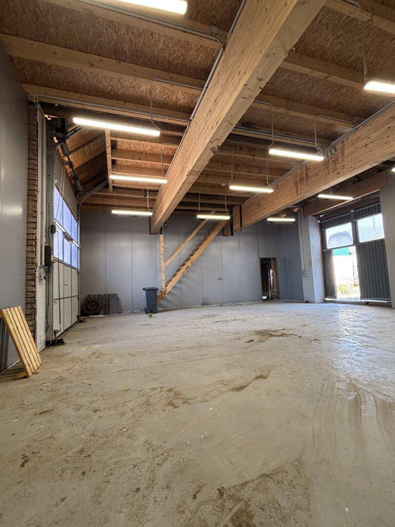 Weitläufige Garage mit viel Tageslicht, Holzbalken und robustem Betonboden.