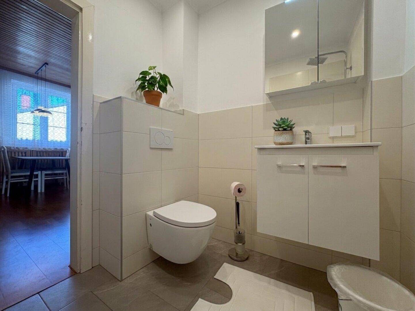 Modernes WC mit wandhängender Toilette, Waschbecken und hellen Fliesen.