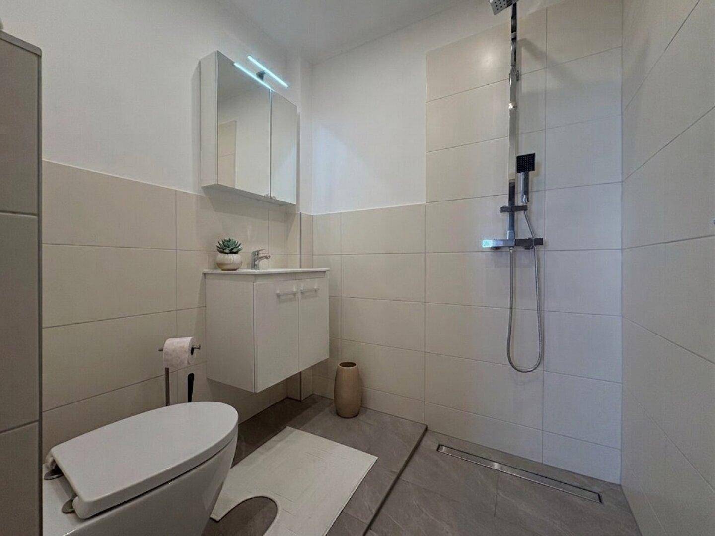 Modernes Badezimmer mit ebenerdiger Dusche, wandhängender Toilette und hellen Fliesen.