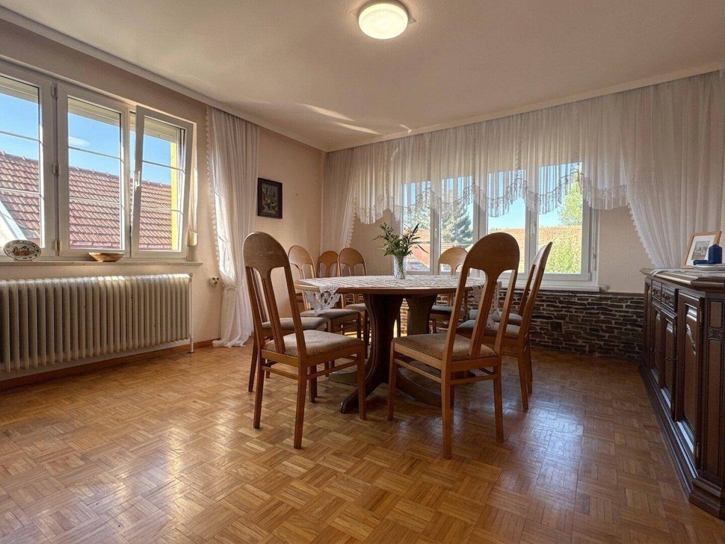 Geräumiges Esszimmer mit Parkettboden, großem Esstisch und vielen Fenstern.