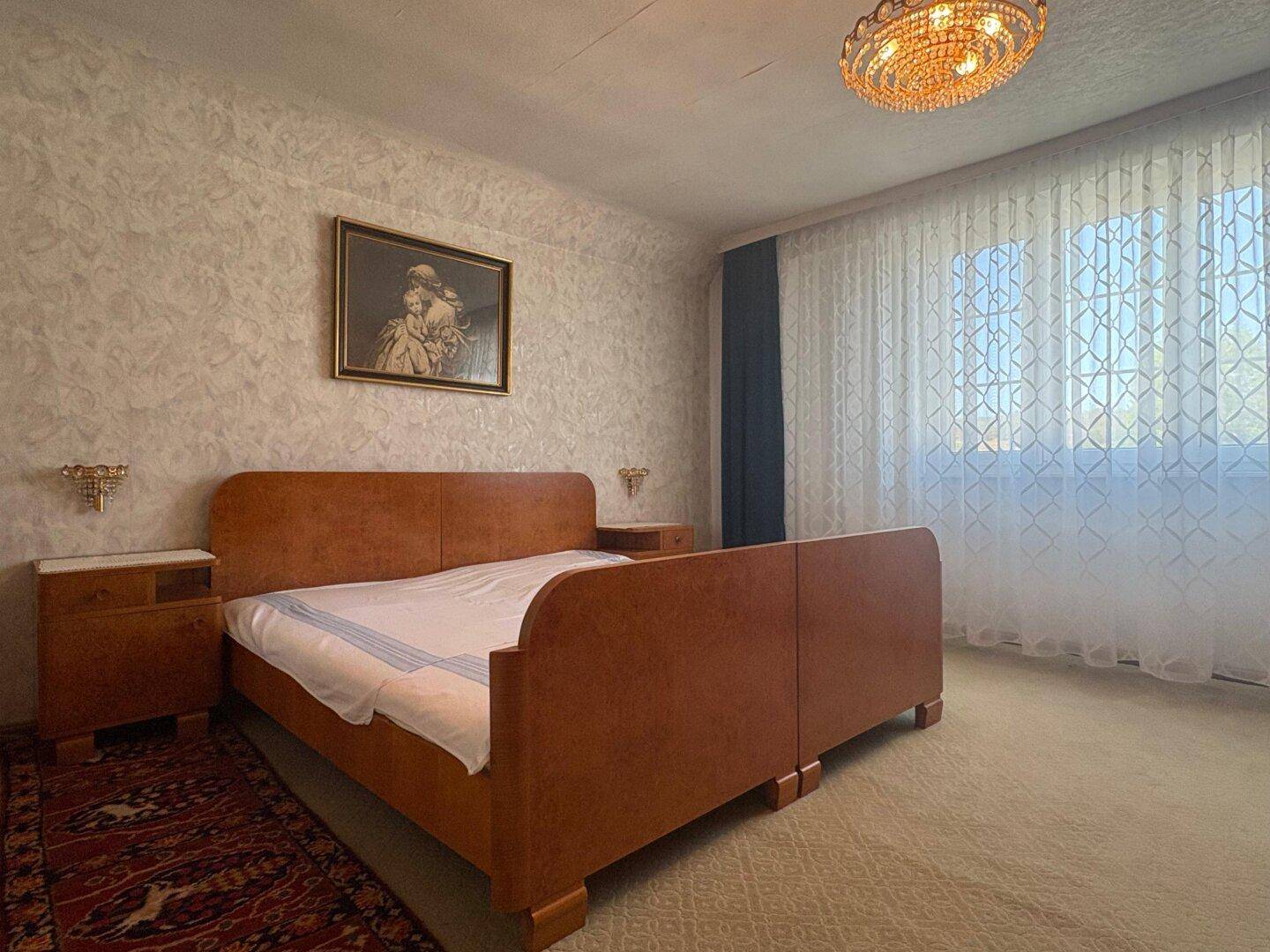 Geräumiges Schlafzimmer mit Doppelbett, Teppichboden und traditionellem Kronleuchter.