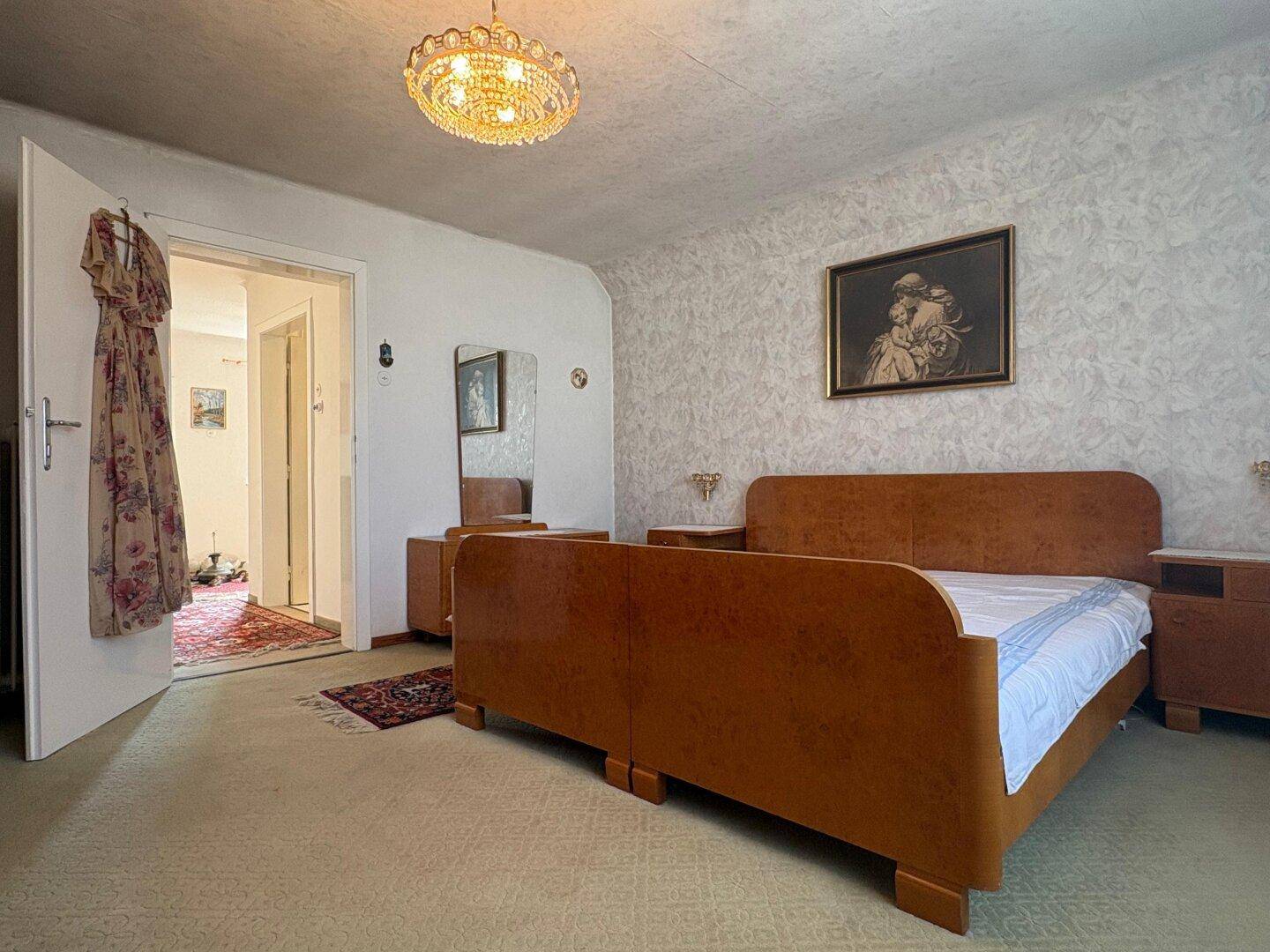 Schlafzimmer mit Doppelbett, Kommode und Zugang zu einem weiteren Raum.