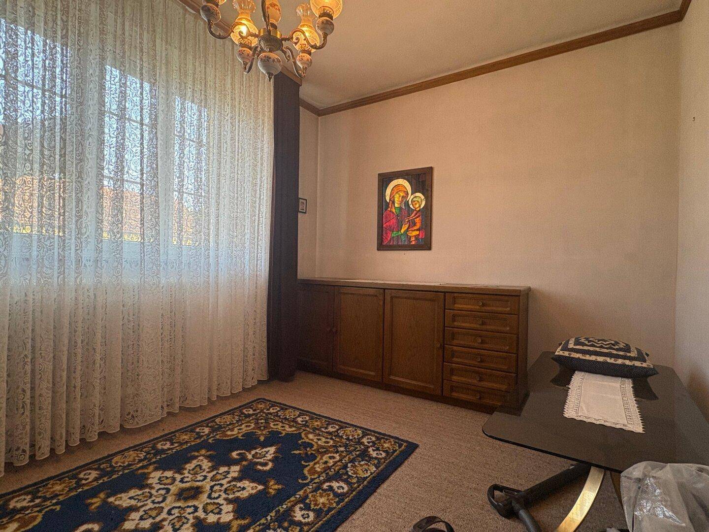 Gemütliches Zimmer mit Teppichboden, Holzschrank und einem Fenster mit Vorhängen.