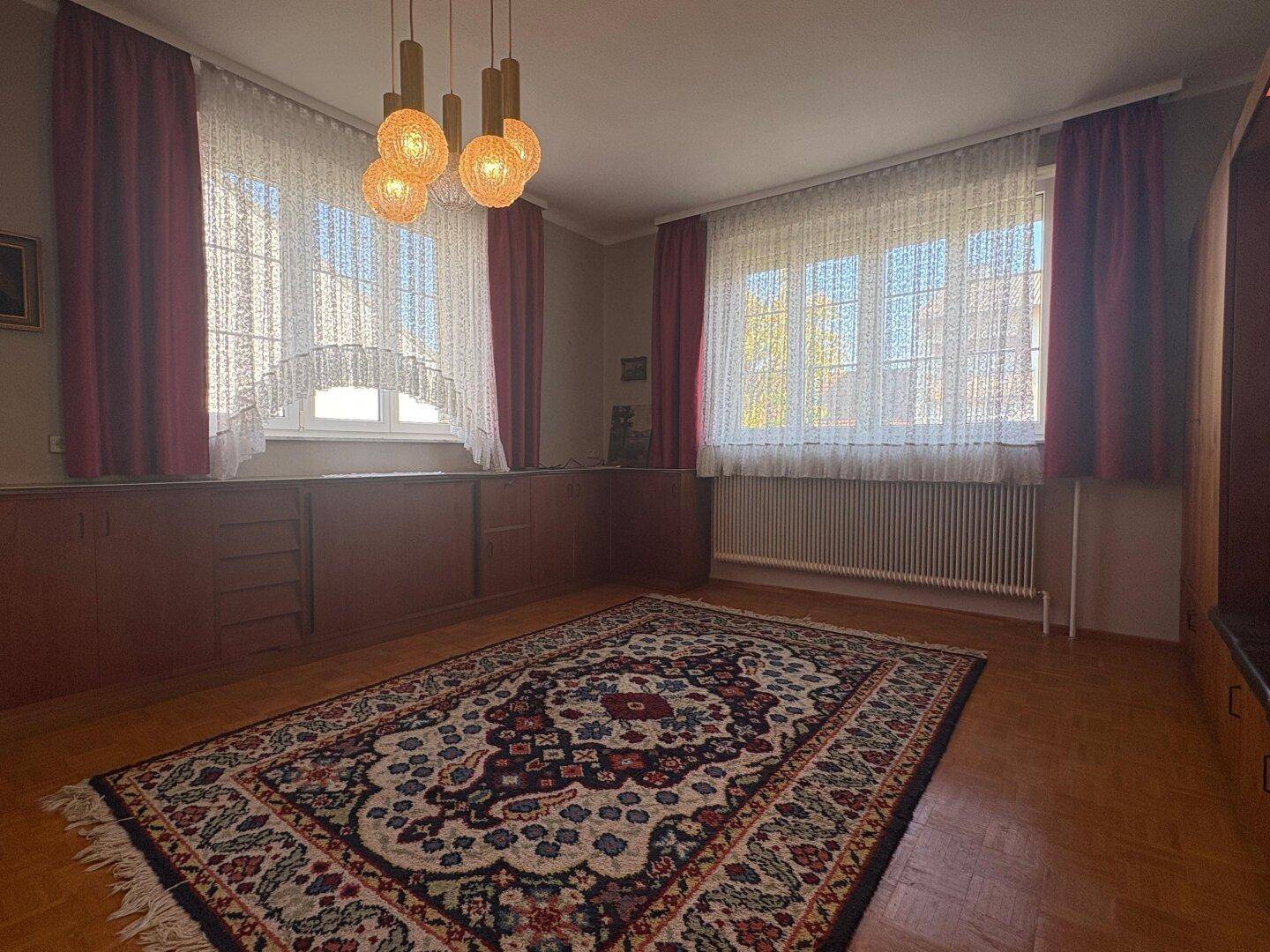 Helles Wohnzimmer mit Parkettboden, großen Fenstern und einem traditionellen Orientteppich.