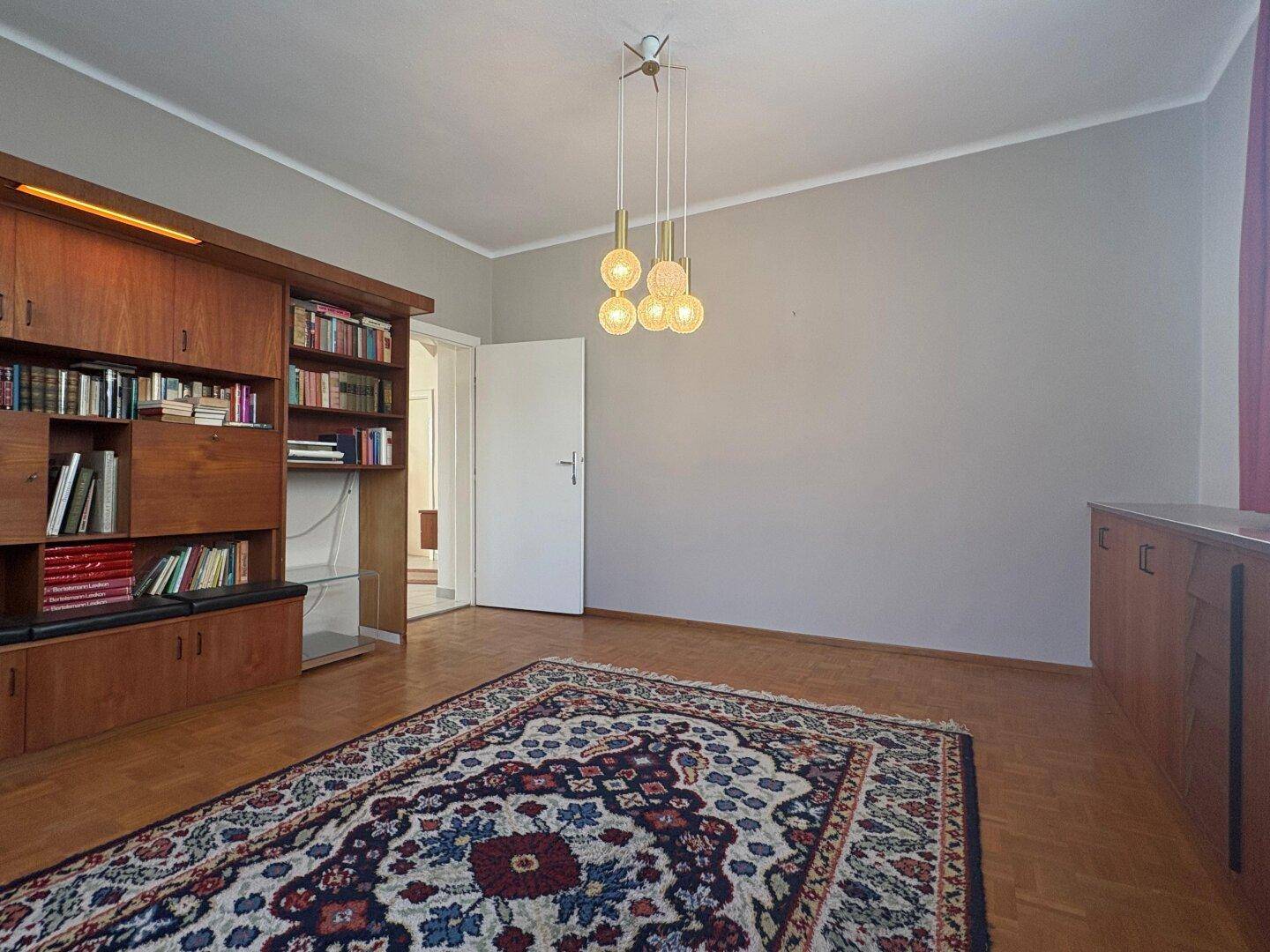 Wohnzimmer mit Holzbücherregal, Parkettboden und schlichter Wandgestaltung.