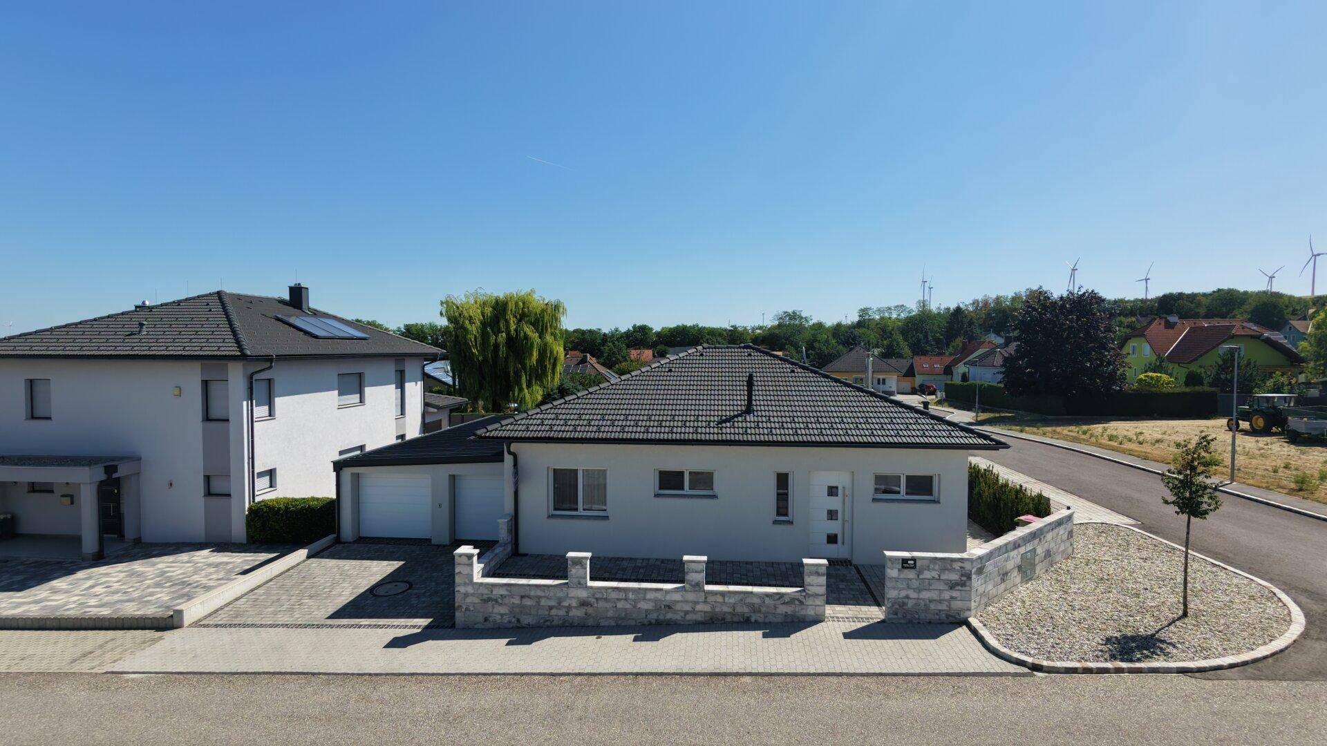 Modernes Einfamilienhaus mit Doppelgarage, gepflasterter Einfahrt und Steinmauer.