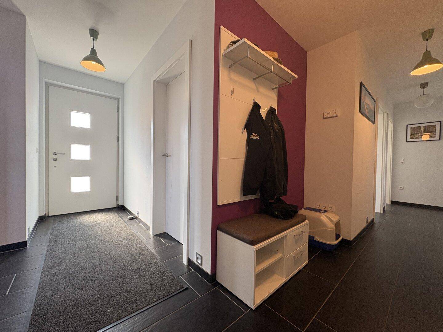 Heller Eingangsbereich mit dunklen Fliesen, Garderobe und lila Akzentwand.