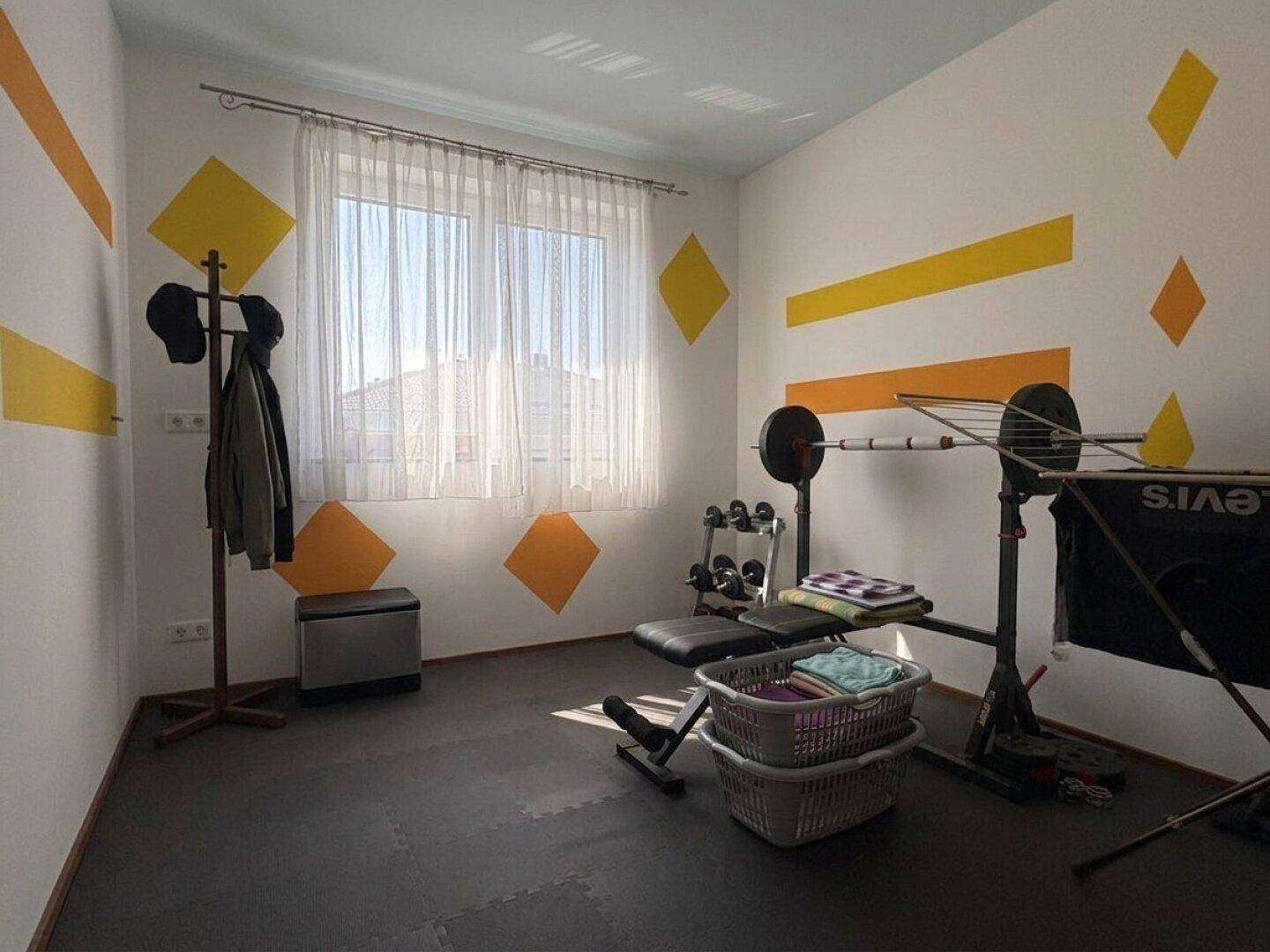 Raum mit Fitnessgeräten, farbigen Akzenten und Blick nach draußen.