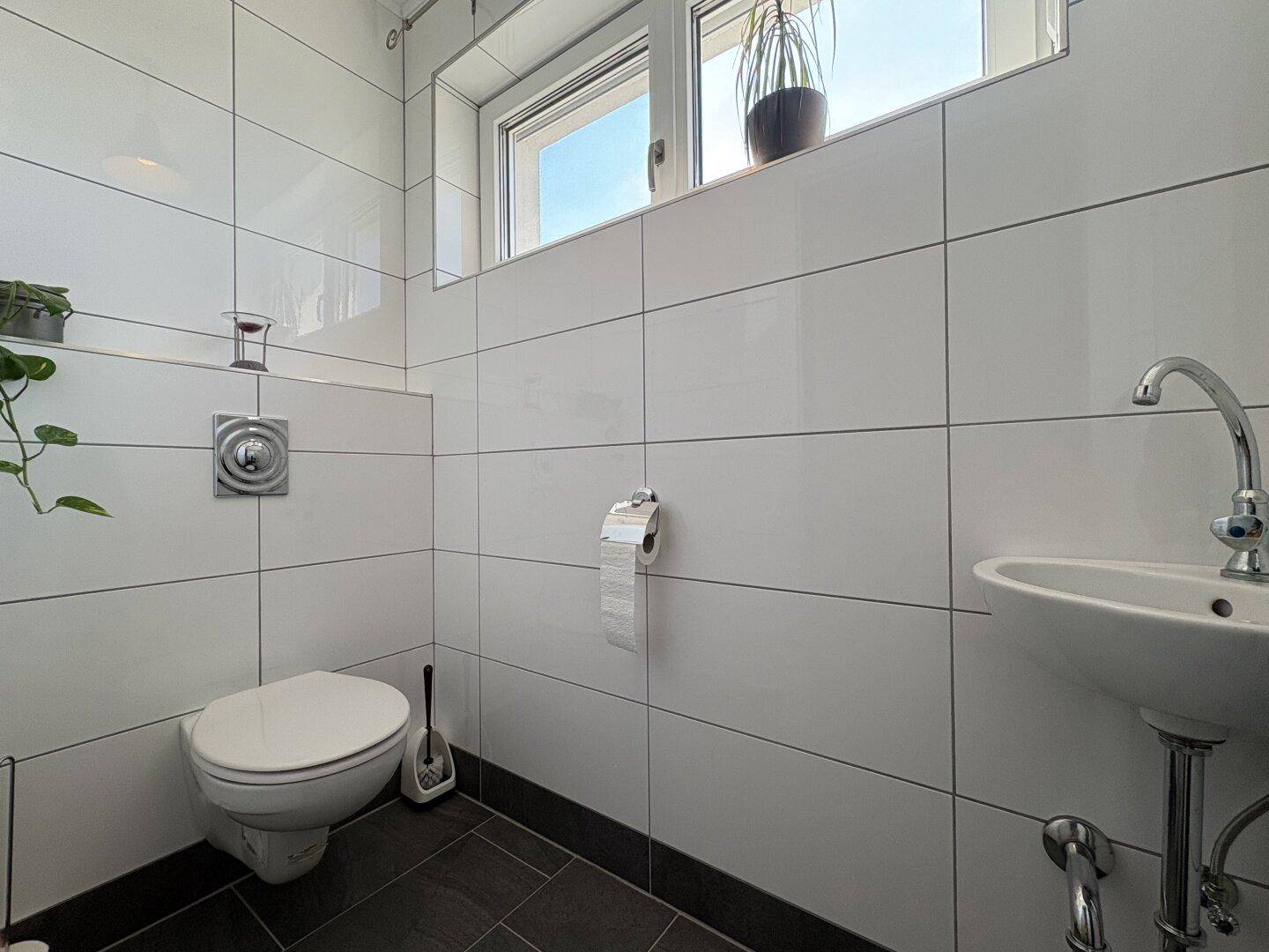 Modernes Gäste-WC mit wandhängendem WC, kleinem Waschbecken und Fenster.
