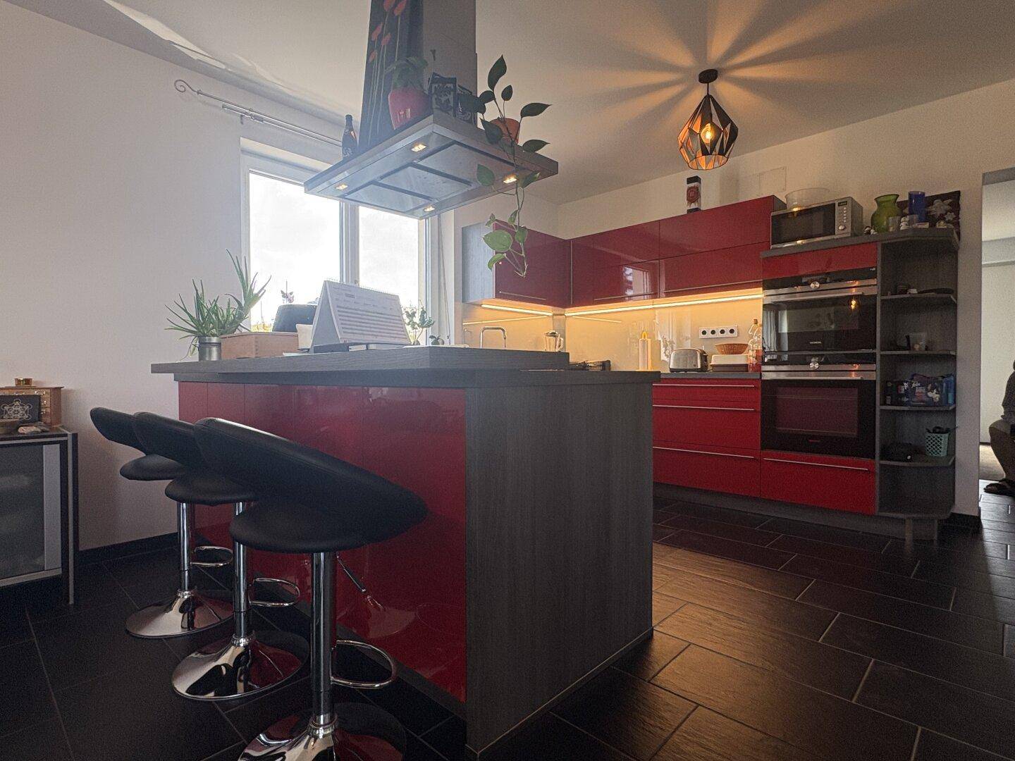 Moderne Küche mit roter Hochglanzfront, Kochinsel und integrierten Geräten.