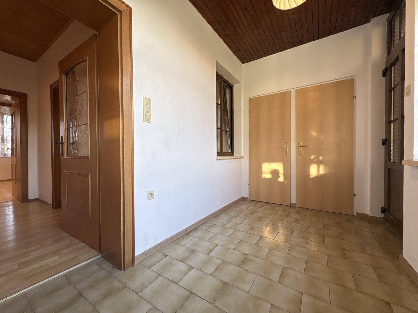Heller Flur mit Fliesenboden, Holztüren und einer Holzdecke, die zum Wohnbereich führt.