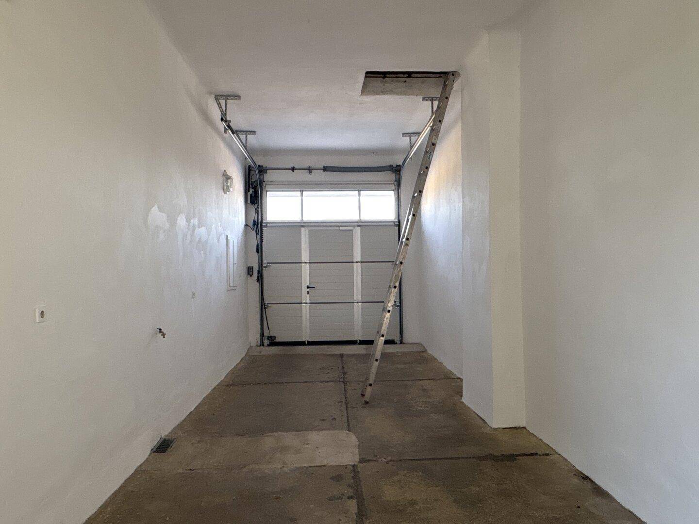 Leere Garage mit Rolltor und Betonboden, bietet Platz für ein Fahrzeug und Lagerung.