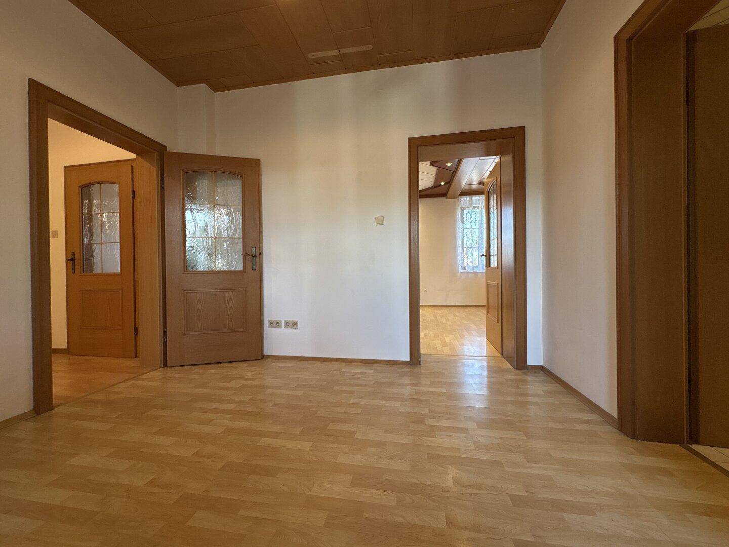 Geräumiger Raum mit Holzboden und mehreren Holztüren, die zu anderen Zimmern führen.