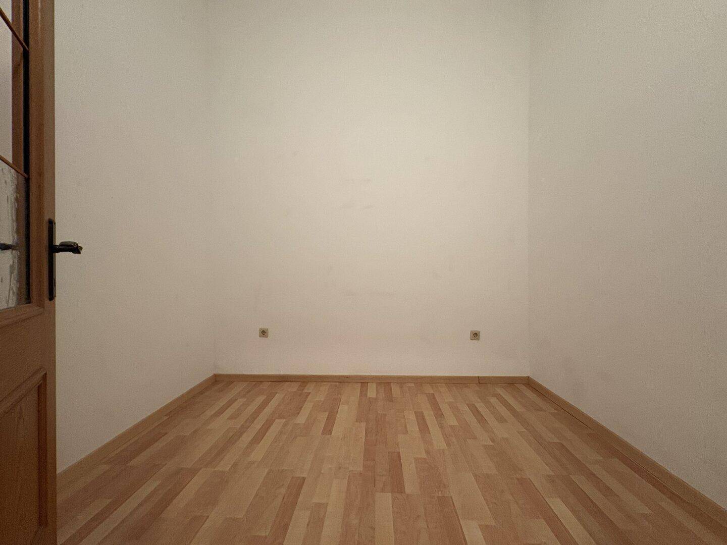 Kleiner, heller Raum mit Holzboden und weißen Wänden, ideal als Kinder- oder Gästezimmer.