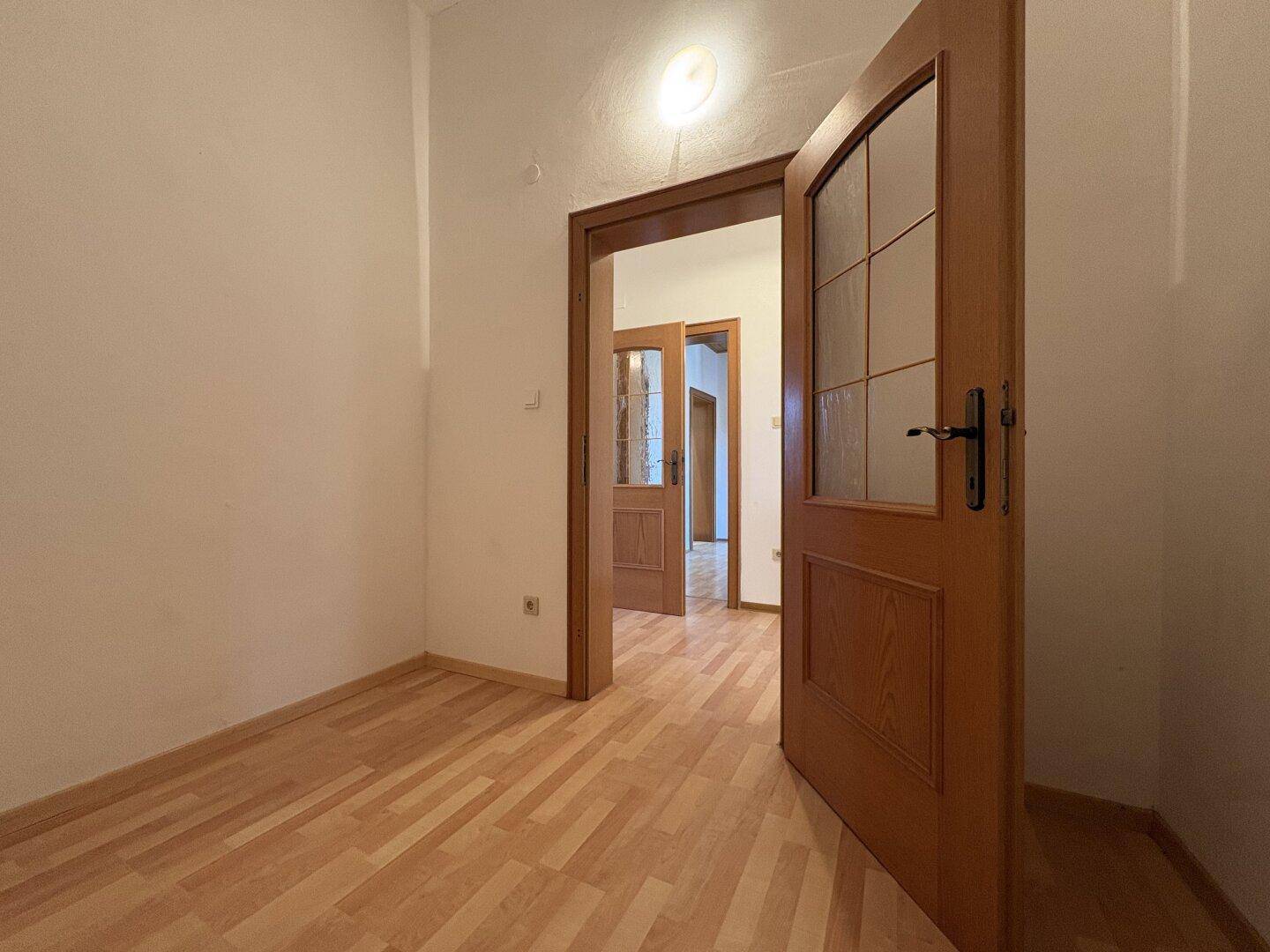 Heller Raum mit Holzboden und Holztüren, die zu weiteren Zimmern im Haus führen.