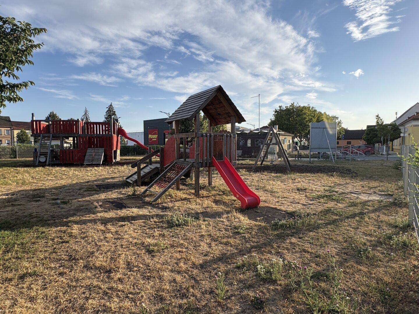 Öffentlicher Spielplatz mit verschiedenen Holzspielgeräten und Rutschen auf trockenem Gras.