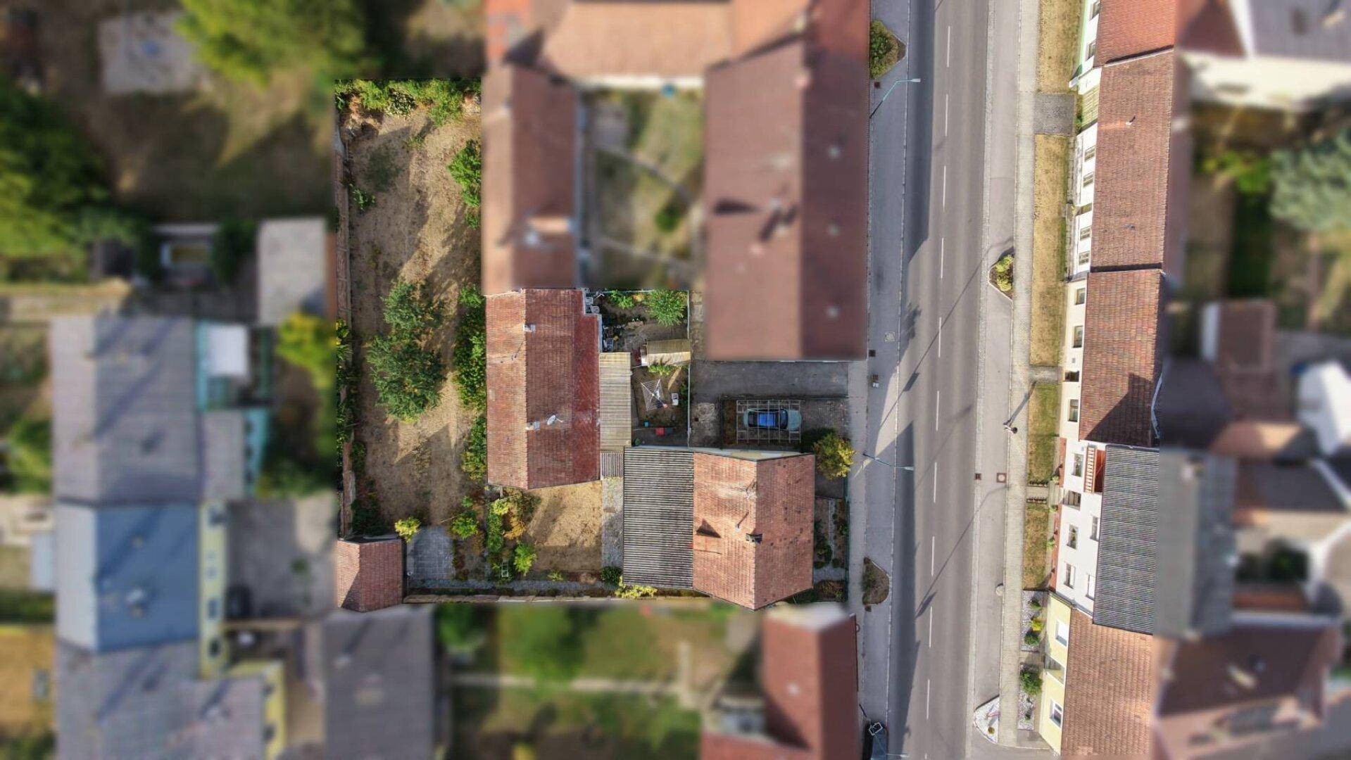 Luftaufnahme eines Wohngebiets mit Häusern, Gärten und einer Straße bei sonnigem Wetter.
