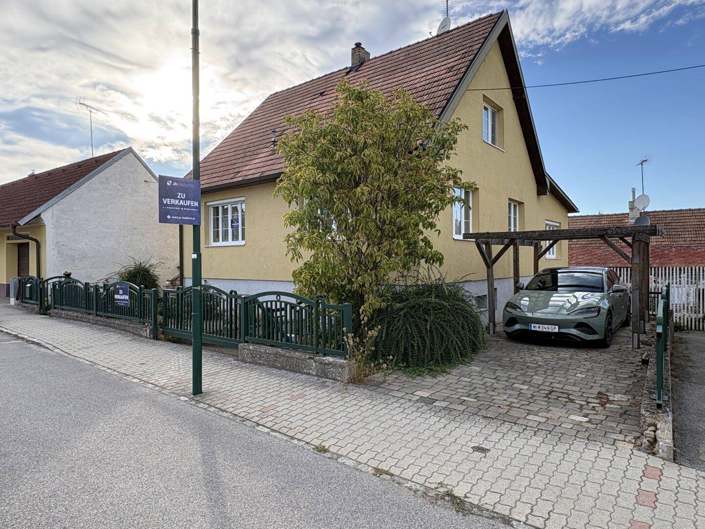 Vorderansicht des Hauses von der Straße mit einem Carport und gepflasterter Einfahrt.