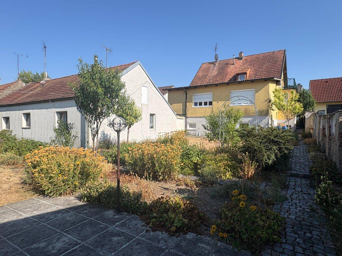 Gepflegter Gartenbereich hinter dem Haus mit verschiedenen Pflanzen und einem gepflasterten Weg.