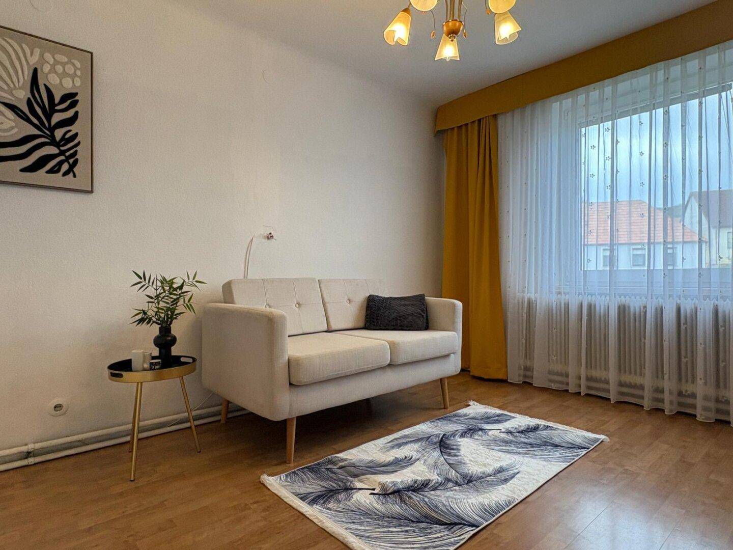 Helles Wohnzimmer mit beigem Sofa, Holzboden und gelben Vorhängen.