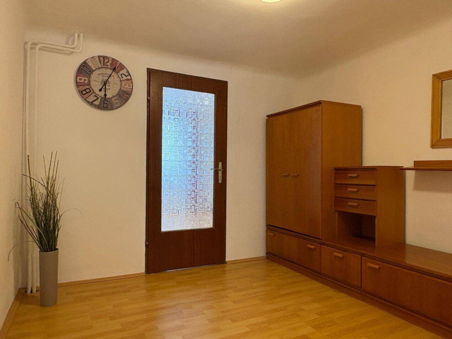 Flur mit Laminatboden, Holzeinbauschrank und dekorativer Wanduhr.