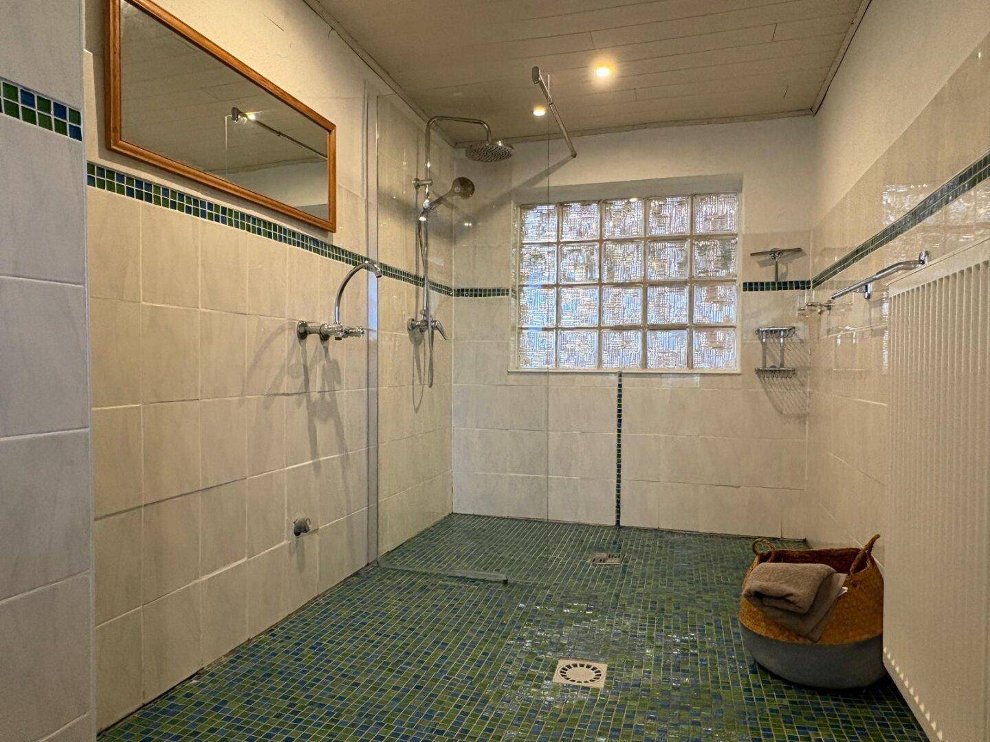 Geräumiges Badezimmer mit grünen Mosaikfliesen und großer begehbarer Dusche.