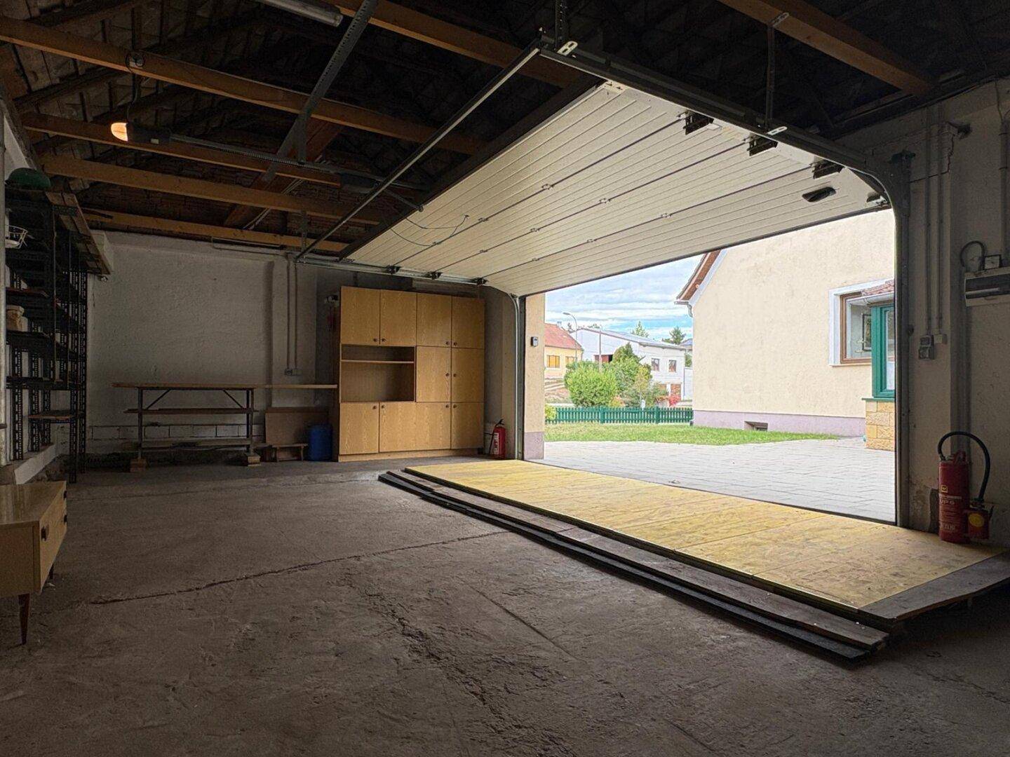 Geräumige Garage mit Betonboden, offenem Garagentor und Blick auf den Außenbereich.