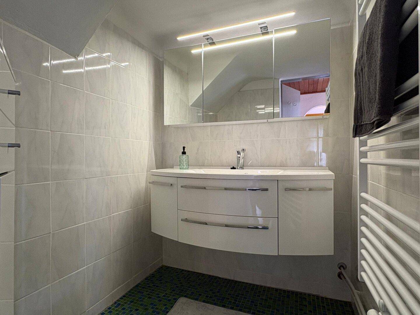 Modernes Badezimmer mit weißem Waschtisch, Spiegelschrank und Handtuchheizkörper.