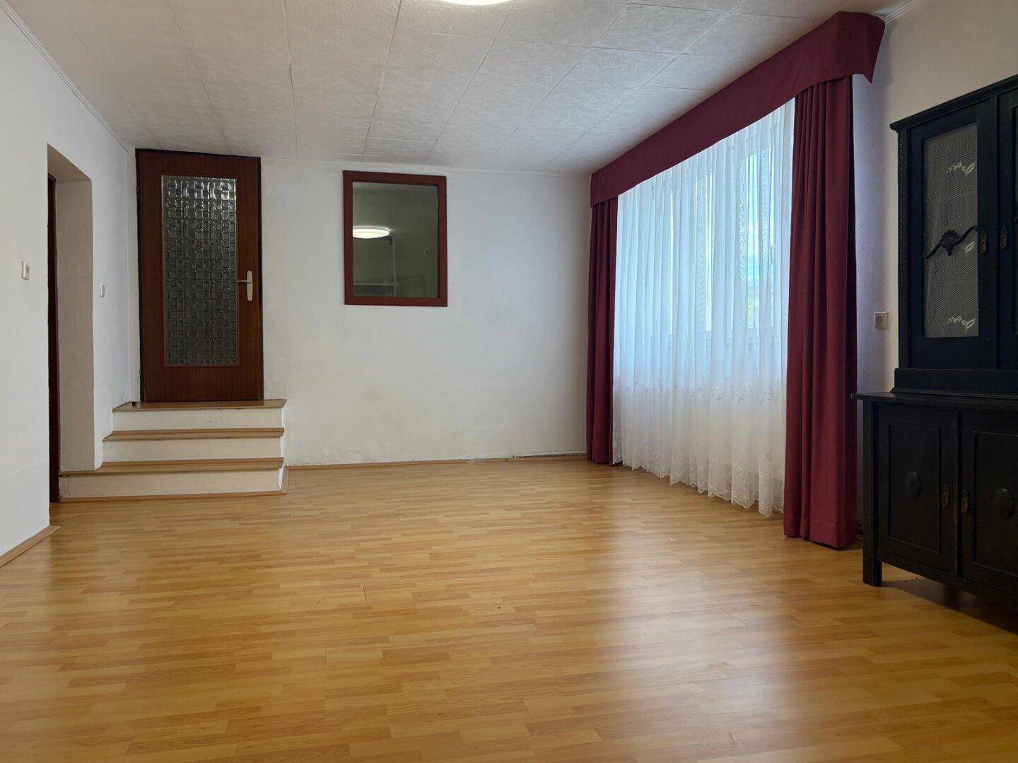 Geräumiges Wohnzimmer mit Laminatboden und Zugang zu einem anderen Raum.