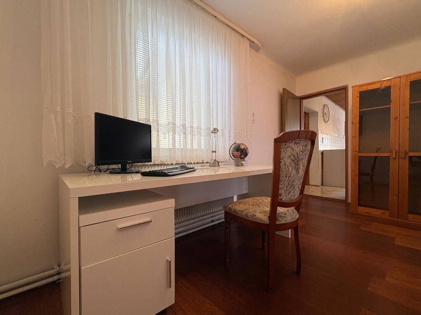 Arbeitszimmer mit Holzboden, weißem Schreibtisch und Blick in den Flur.