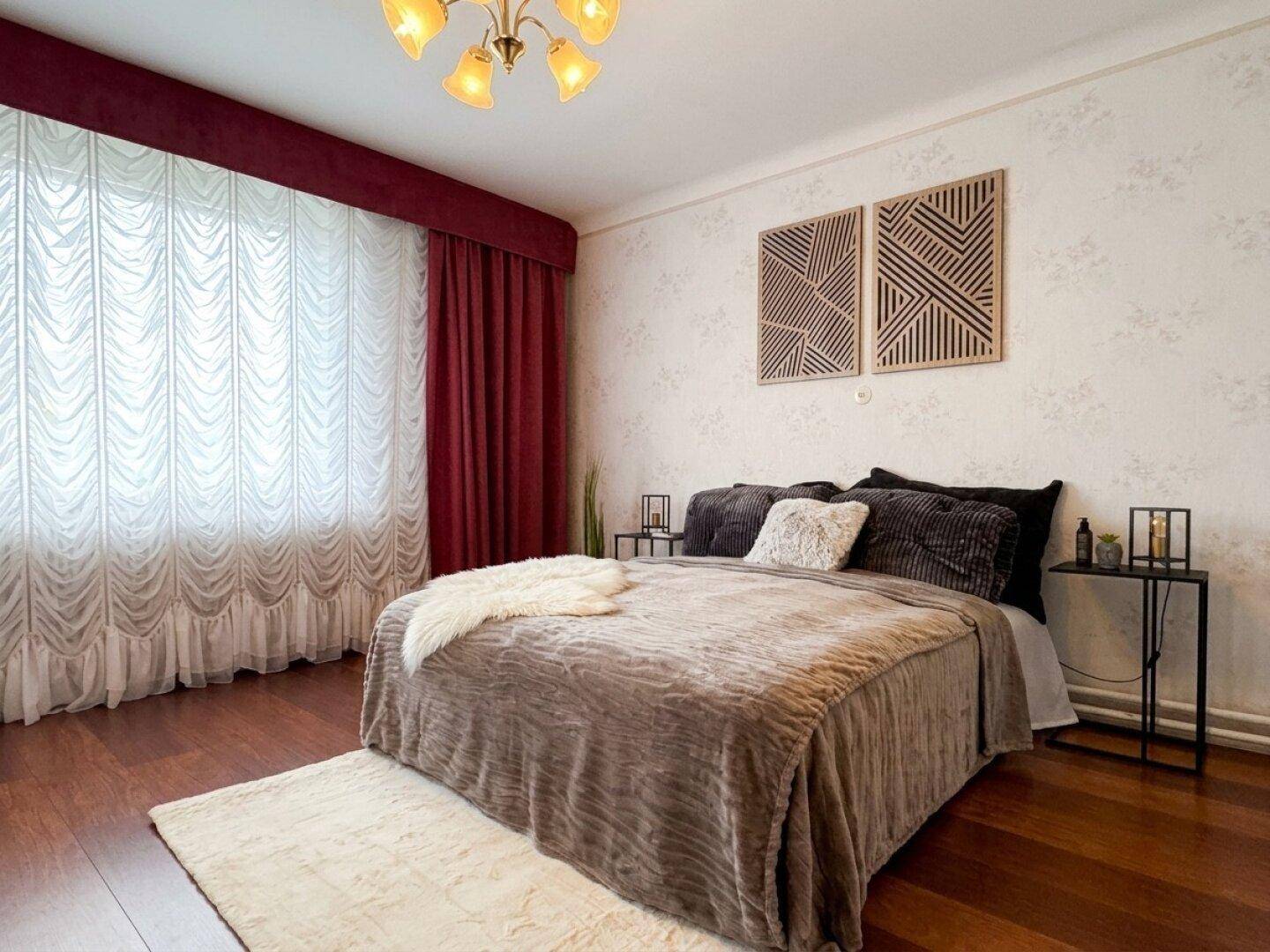 Gemütliches Schlafzimmer mit Holzboden, großem Bett und roten Vorhängen.