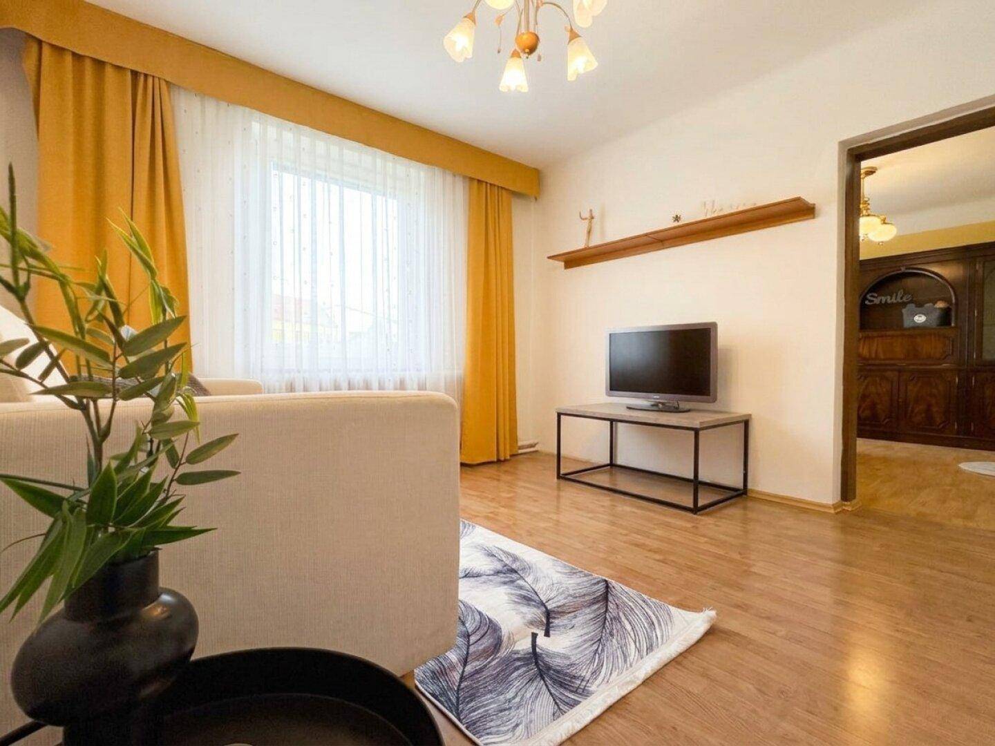 Wohnzimmer mit Holzboden, Fernseher und Blick in einen angrenzenden Raum.