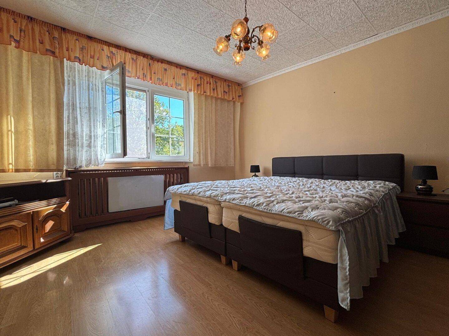 Schlafzimmer mit Doppelbett, Holzmöbeln und Fenster mit Vorhängen.