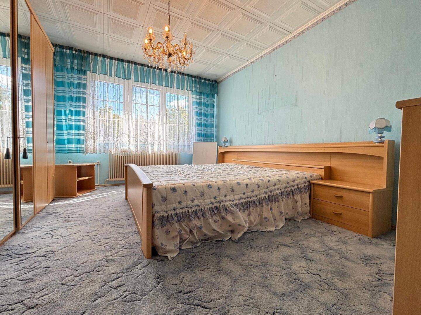 Schlafzimmer mit Doppelbett, Spiegelschrank und blauen Vorhängen.