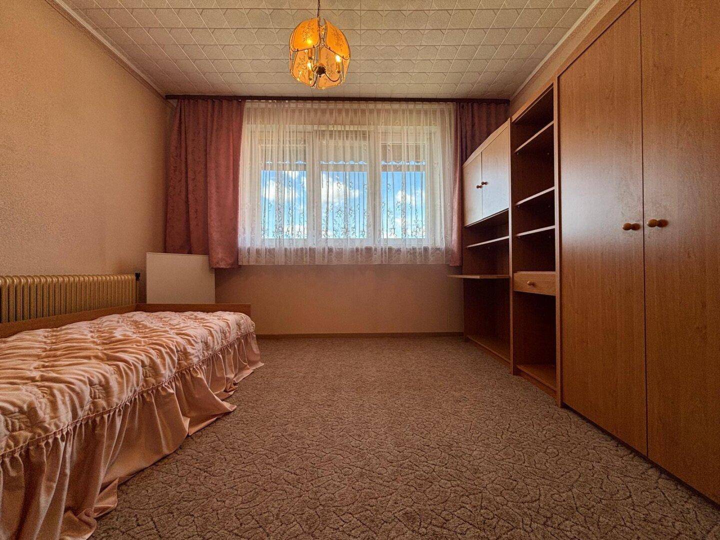 Schlafzimmer mit Einzelbett, Teppichboden und Holzschrank.