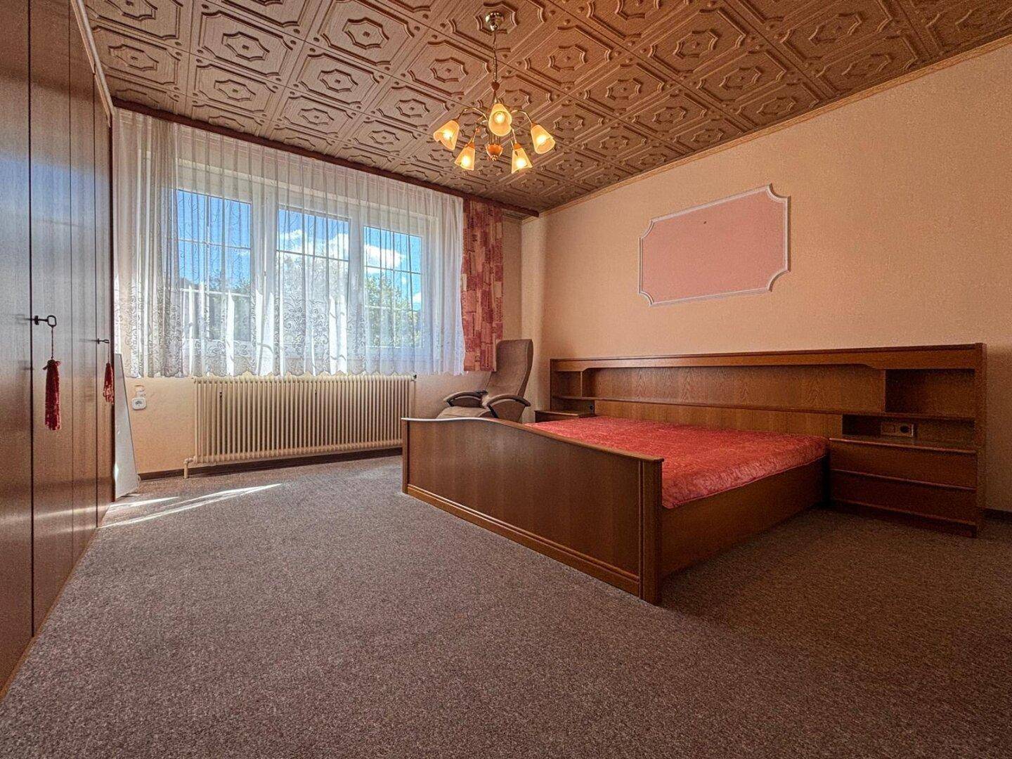 Schlafzimmer mit Doppelbett, Teppichboden und großem Fenster.
