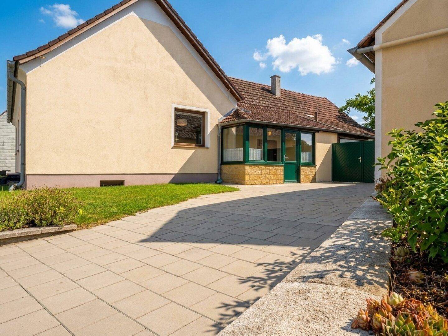 Gepflasterte Einfahrt neben dem Haus mit Rasenfläche und Sträuchern.