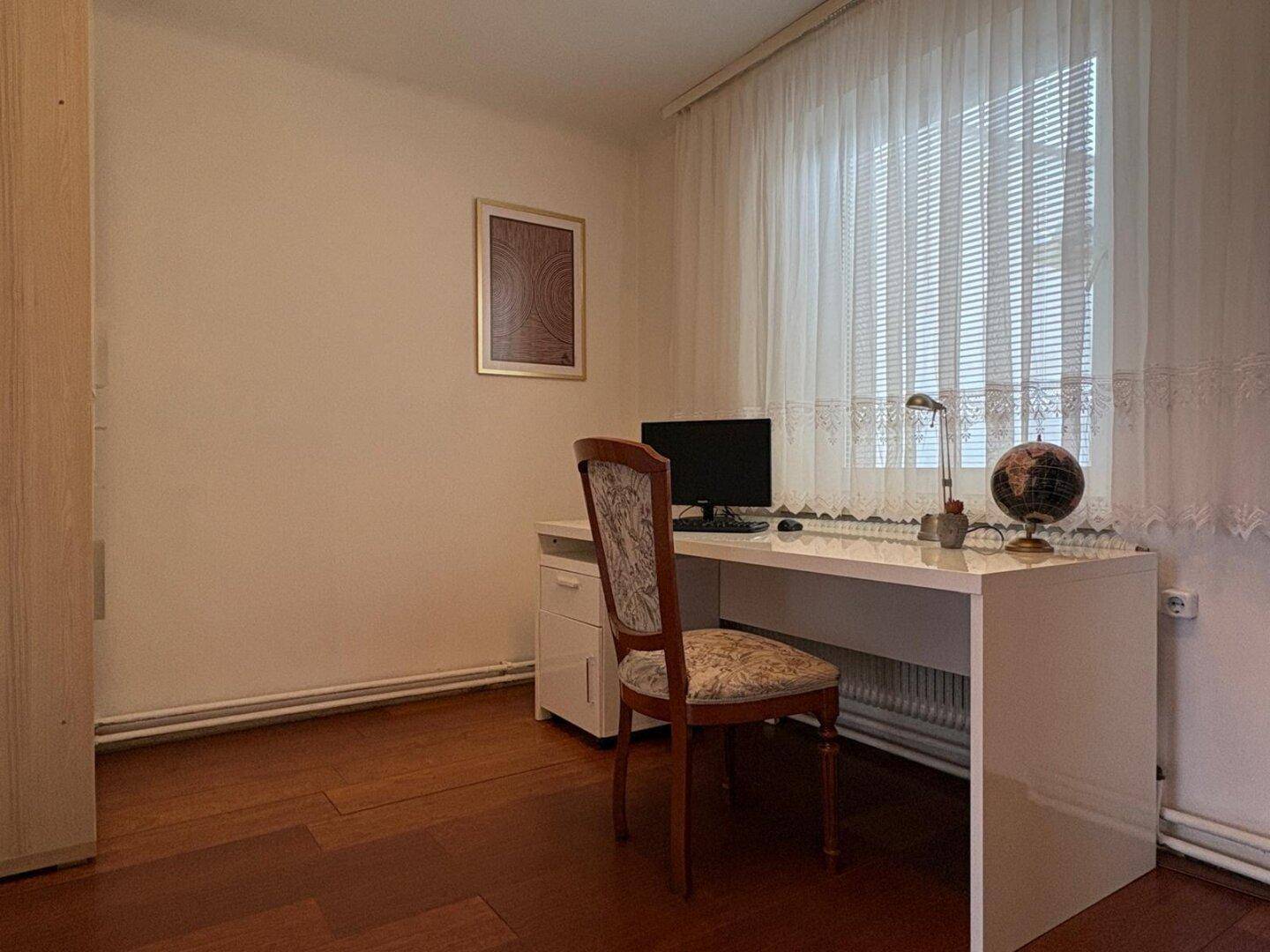 Helles Arbeitszimmer mit weißem Schreibtisch, Bürostuhl und großem Fenster.