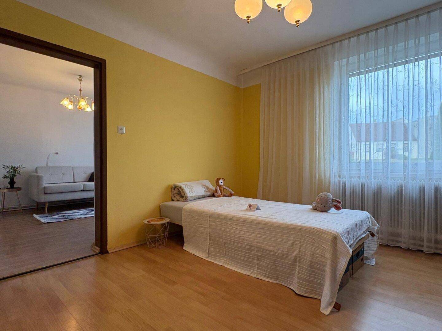 Schlafzimmer mit gelber Wand, Einzelbett und Zugang zum Wohnzimmer.
