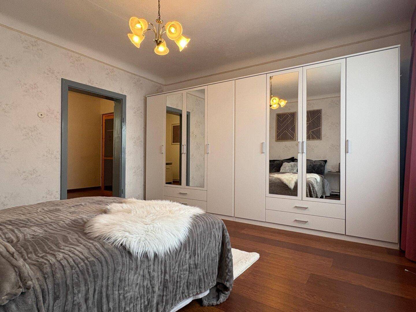 Schlafzimmer mit Holzboden und großem weißen Kleiderschrank mit Spiegeltüren.