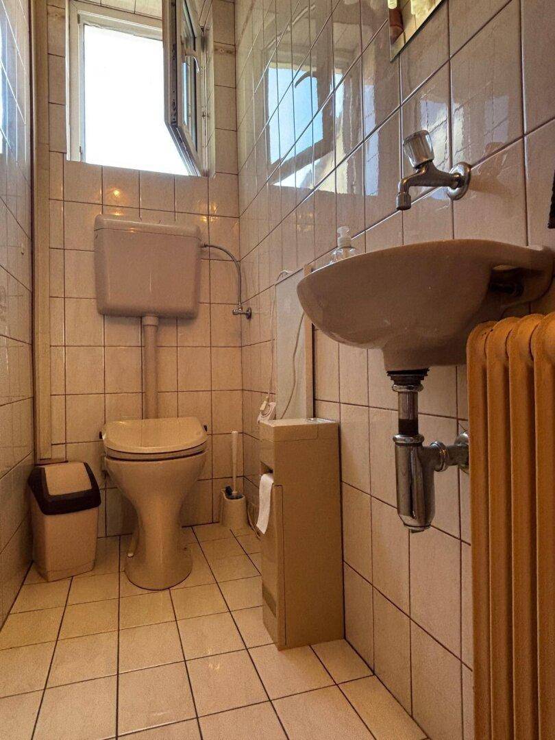 Kleines WC mit beigen Fliesen, Toilette und Waschbecken.