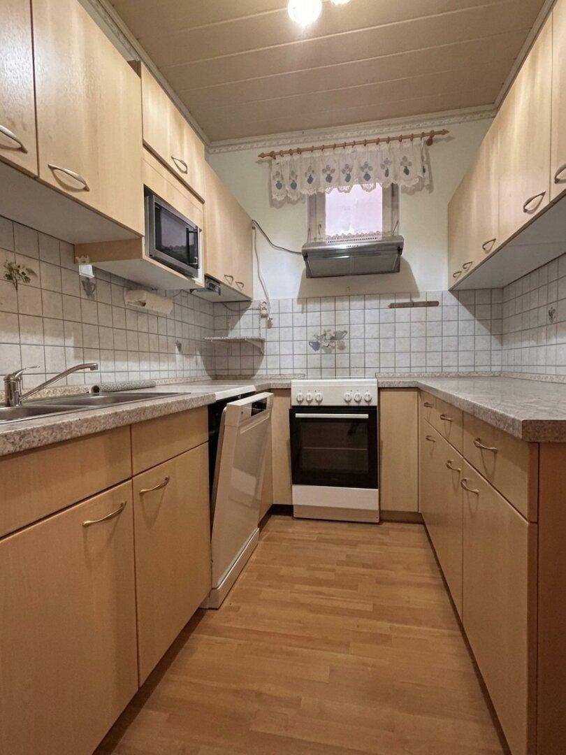 Funktionale Küche mit hellen Holzschränken, Fliesenrückwand und Geräten.