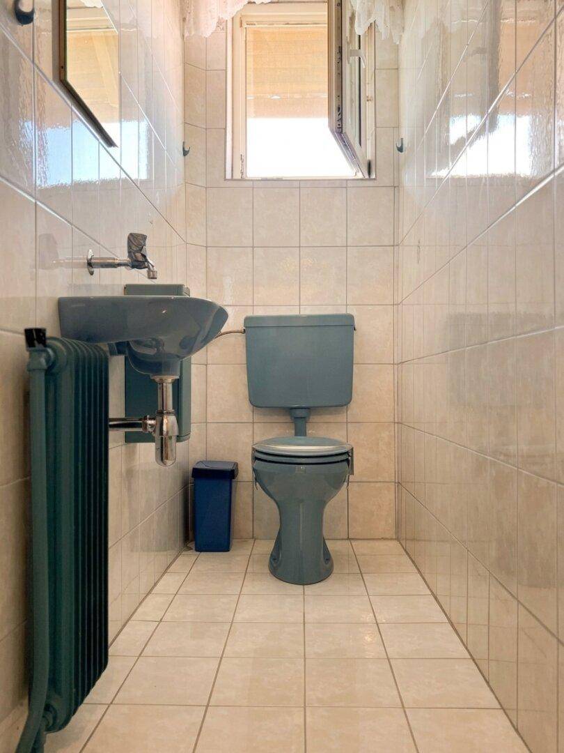 Kleines WC mit blauen Sanitärobjekten und hellen Fliesen.