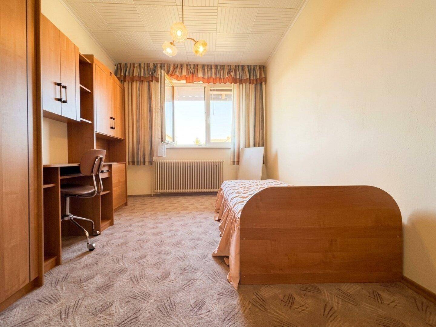 Zimmer mit Schreibtisch, Einzelbett und Teppichboden.